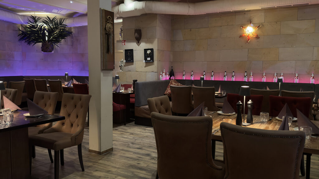 Ein modernes Restaurant mit braunen, getufteten Stühlen, Holztischen zum Essen, gepolsterten Stühlen, Wandkunst und farbiger Stimmungsbeleuchtung an der Rückwand.