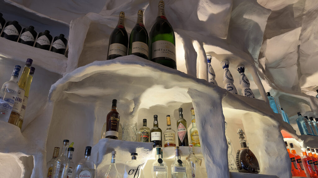 Auf weißen, höhlenartigen Regalen stehen Flaschen mit verschiedenen Spirituosen und Weinen, darunter große Flaschen mit Champagner von Moët & Chandon und verschiedene andere Spirituosen, die von einer sanften Beleuchtung angestrahlt werden.